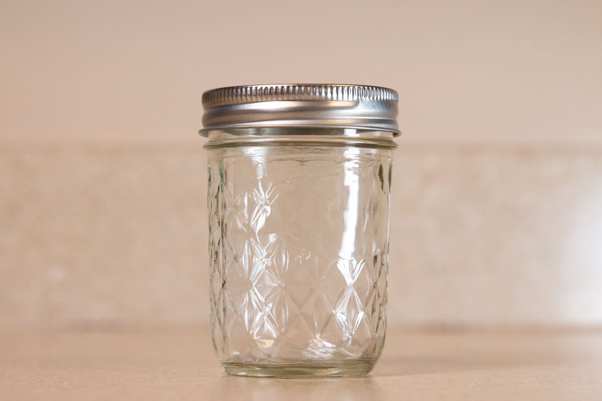 An empty clear glass jar used as the base for a plastic-wrap fruit fly trap
